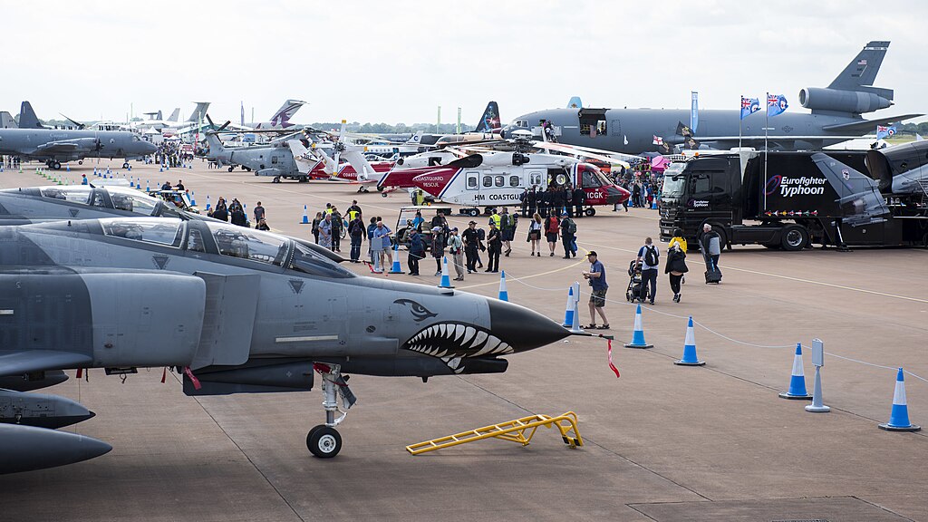 crowds explore military aeroplanes and helicopters on display at the royal international air tattoo airshow, with barriers and exhibits visible.