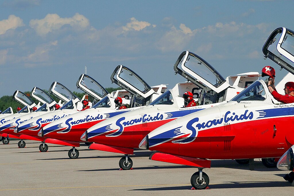 row of red and white snowbirds aeroplanes in montreal, 2026, parked on the tarmac with cockpits open and pilots inside.