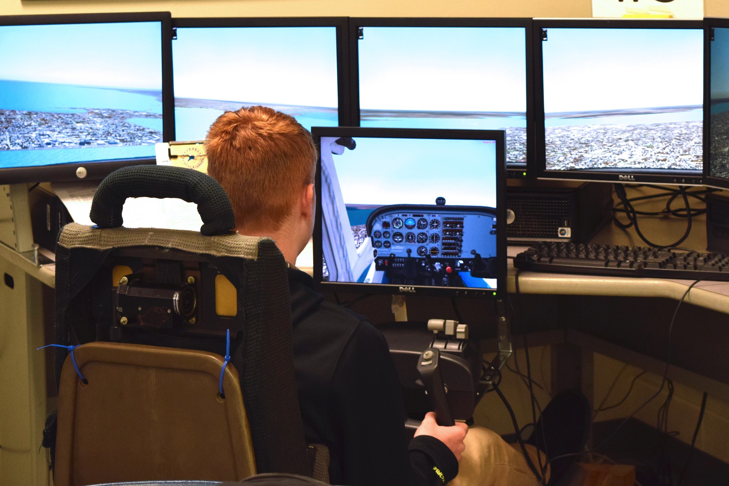 Student flying a desktop flight simulator with multi-screen visuals