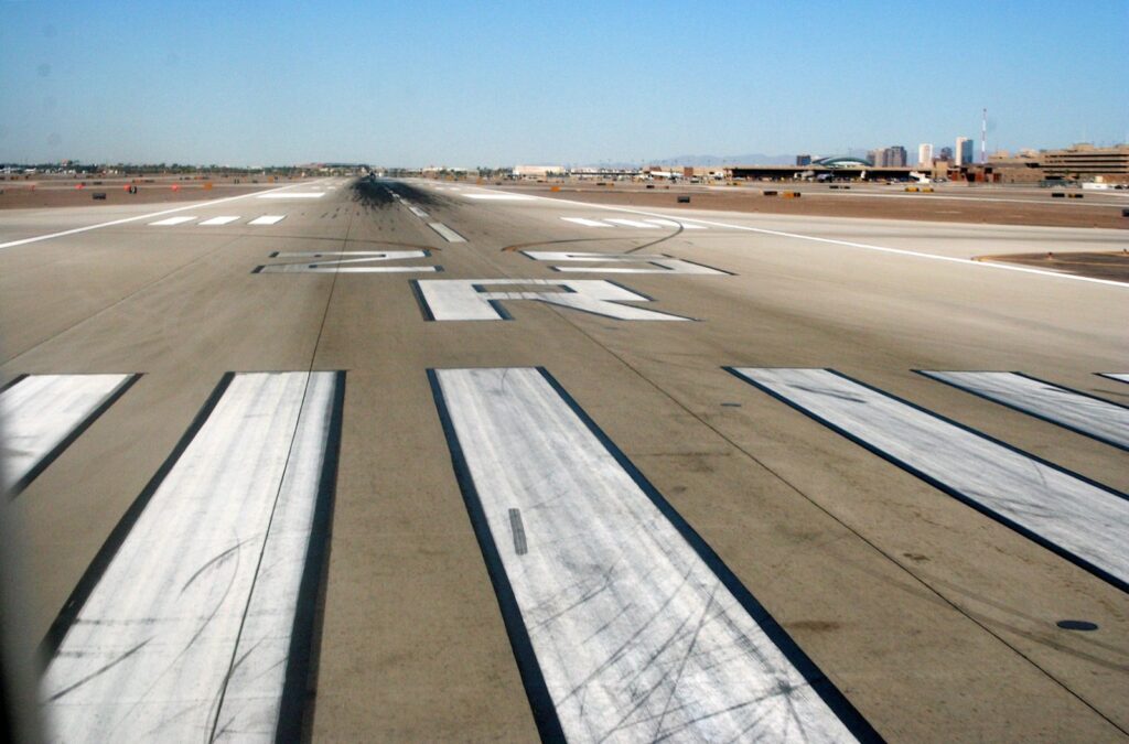 Runway 25R threshold at Phoenix Sky Harbor: white threshold stripes outlined in black, the runway designation number and letter, and the centreline beyond.